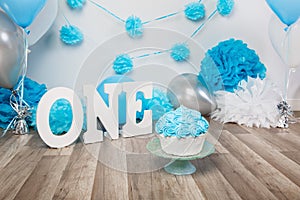 Festive background decoration for birthday celebration with gourmet cake, letters saying one and blue balloons in studio