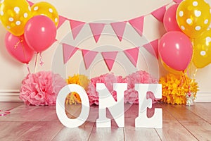 Festive background decoration for birthday celebration with letters saying one and pink red yellow balloons