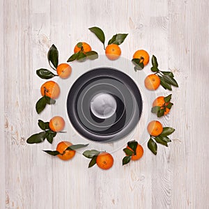 Festive background from mandarins with leaves and black empty plates and bowl