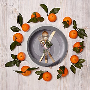 Festive background from mandarins with leaves and plate with cutlery set