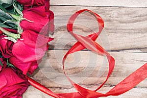 Festive background for March 8, World Women`s Day. Red roses and a red ribbon in the form of the figure eight, on a wooden backgro