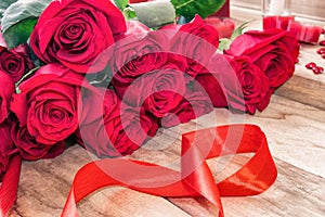 Festive background for March 8, World Women`s Day. Red roses and a red ribbon in the form of the figure eight, on a wooden backgro