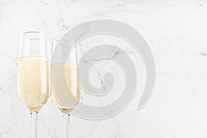 Festive background with sparkling champagne in two glasses on white soft light  marble backdrop, closeup, top part. Holiday drink.