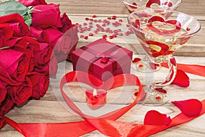 Festive background to the Valentine`s day. A bouquet of red roses, a gift box, a heart-shaped candle and a red ribbon with a heart