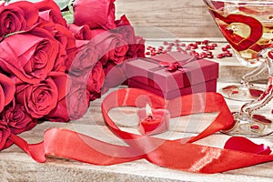 Festive background to the Valentine`s day. A bouquet of red roses, a gift box, a heart-shaped candle and a red ribbon with a heart