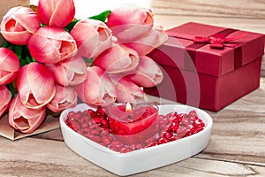 Festive background to the Valentine`s day. A bouquet of tulips, a gift box, a heart-shaped plate and a heart-shaped candle.