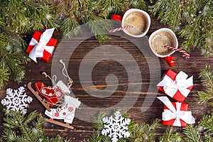 Festive background with two coffee mugs, fir branches, toy skates and gifts on wooden table