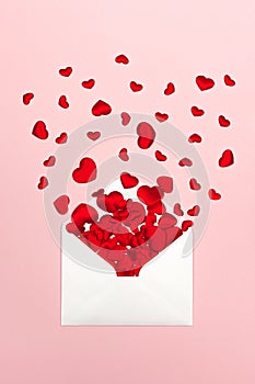 Festive background for Valentine`s day with red hearts scattered from envelope on pink background.