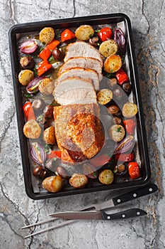 Festive baked pork loin with potatoes, onions, peppers and mushrooms close-up on a baking sheet. Vertical top view