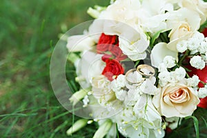 Festive beautiful bouquet of red and white flowers on green grass with wedding rings