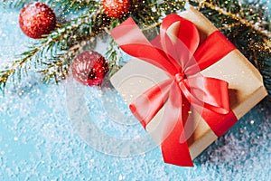 Festive box with a red bow close-up on a blue background with Christmas toys balls a branch of fluffy spruce sparkles