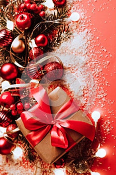 Festive boxes with a satin red bow on a red background with Christmas toys balls, a branch of fluffy fir tree, sparkles