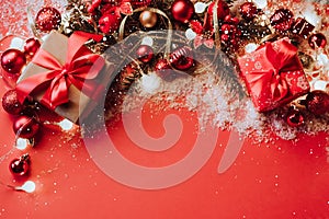 Festive boxes with a satin red bow on a red background with Christmas toys balls, a branch of fluffy fir tree, sparkles