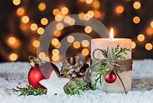 Festive Christmas holiday celebration candle on snow with xmas ornaments decoration and lights background