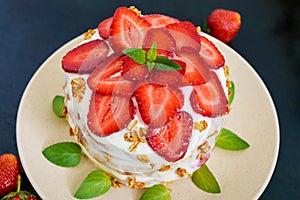 A festive cake with fresh strawberries, cream, decorated with mint leaves on a black background.