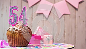 Festive cake or muffin with a pink candle with a number 54. Happy birthday background with a number for a girl or woman with