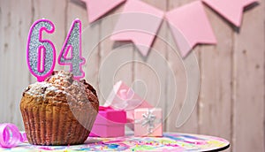 Festive cake or muffin with a pink candle with a number 64. Happy birthday background with a number for a girl or woman with
