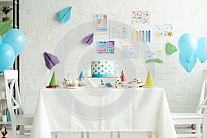 Festive cake and party caps on table in room decorated for birthday party with air balloons.