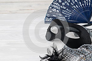 Festive carnival accessories, satin black mask, elegant vintage fan and jewelry on a white background. Flat lay with copy space