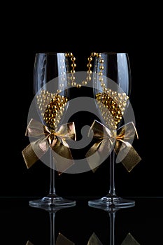 Festive champagne glasses with golden bows and beads on a glass table