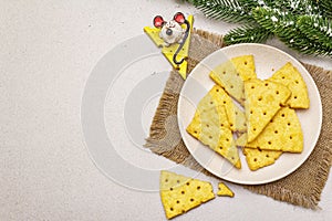 Festive cheese crackers, New Year snack concept. Cookies, mouse figure, fir tree branch, artificial snow, sackcloth napkin. Stone