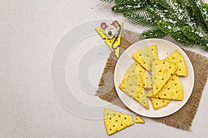 Festive cheese crackers, New Year snack concept. Cookies, mouse figure, fir tree branch, artificial snow, sackcloth napkin. Stone