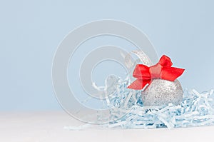 Festive christmas background - silver shiny ball with red ribbon on white wood table and pastel blue wall.