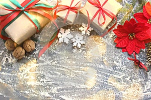 Festive Christmas composition with gifts, boxes, cones, walnuts, red flowers of poinsettia on a wooden background with white sprin