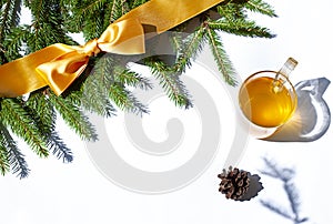 Festive Christmas concept frame with fir and a yellow bow with a cup of green tea on the white background.