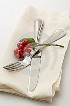 Festive Christmas dinner table setting place setting with silverware fork and knife on cloth napkin with holly berries decorations
