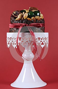 Festive Christmas food, fruit cake with glace cherries and nuts on white cake against a red background