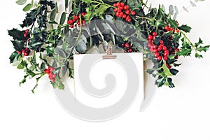 Festive Christmas mockup scene. Greeting card with golden paper binder clip, eucalyptus and holly red berries, leaves