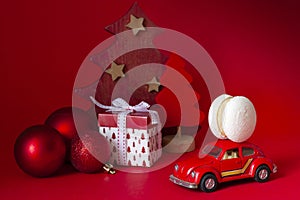 Festive Christmas New Year composition in red with balls and toy car model with french macaroon cookie on red background