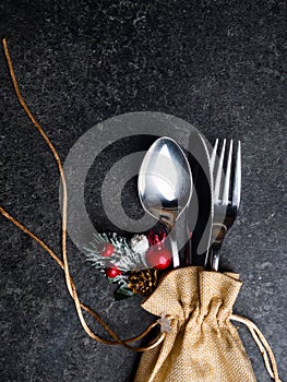 Festive Christmas table place setting with cutlery, pine branche, red berries, rose hip, cone in burlap bag. Winter holidays and