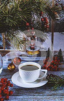 Festive Christmas toy Santa Claus. White cup of coffee on a festive Christmas background. Sweets and Christmas tree branches.