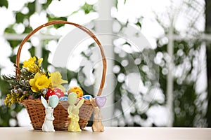 Festive composition with Easter eggs in wicker basket on table against window, space for text