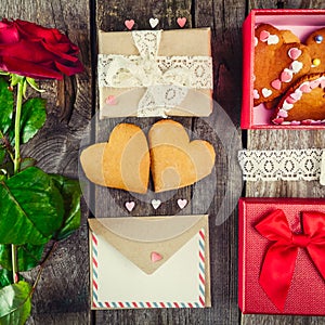 Festive composition with homemade cookies in shape of heart, rose flower, gift box. card with envelope, vintage ribbon. Gift for l