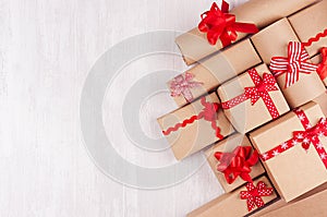 Festive craft paper gifts with red bows closeup on soft white wood board, top view, border.