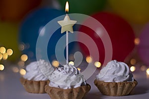 Festive cupcakes with a yellow star-shaped candle. On the background - multi-colored balloons and lights. party