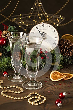 Festive decorated Christmas table with two glasses of champagne, old clock with decorations, fir branches with pine cones, festive