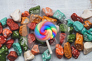 Festive decoration. lollipop and candy pebbles. sweets in the form of colored stones. white woooden background with colorful