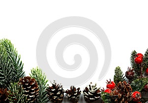 Festive Christmas composition with snow covered evergreen branches, pine cones and red berries on white background.