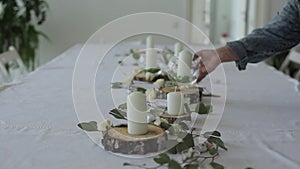 Festive design of the wedding table. A woman places glass vases with candles on wooden circles among flowers. Close-up