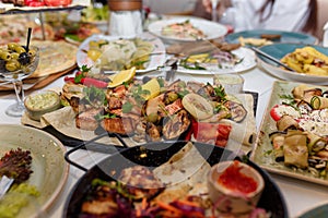 Festive dishes with grilled meat and vegetables, tomato, lemon, vegetable salads, olives decorated with parsley. Wedding