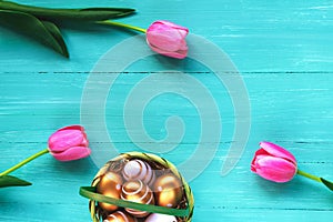 Festive Easter background. Pink tulips and golden painted eggs on a turquoise wooden table.
