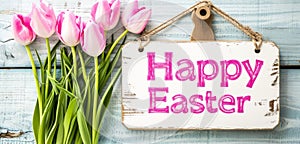 A festive Easter display with pink tulips and a Happy Easter sign on a rustic wooden background. Ideal for seasonal