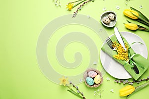 Festive Easter table setting with eggs and floral decor on green background, flat lay. Space for text