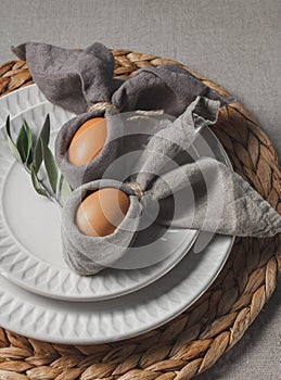 Festive Easter table setting. Funny Easter bunny made of eggs and linen napkin on plate. Gray background