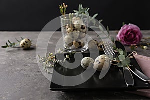 Festive Easter table setting with quail eggs and floral decoration on dark background