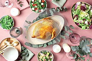 Festive family dinner table. Serving plates, bowls with salads and vegetables dishes, snack, whole roasted chicken, eucalyptus